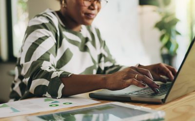Closeup of a woman working on a laptop with financial documents on her desk