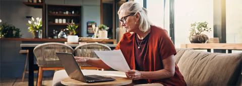 Retired woman reviewing documents in front of her laptop.